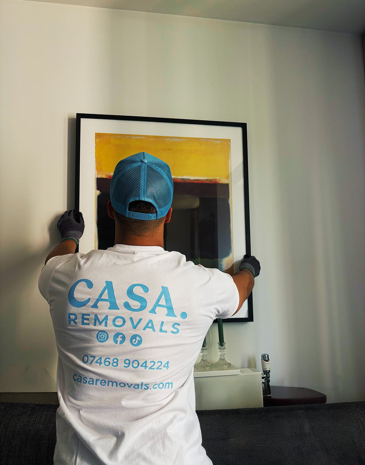 A uniformed CASA. crew member carefully hanging framed art in a London home
